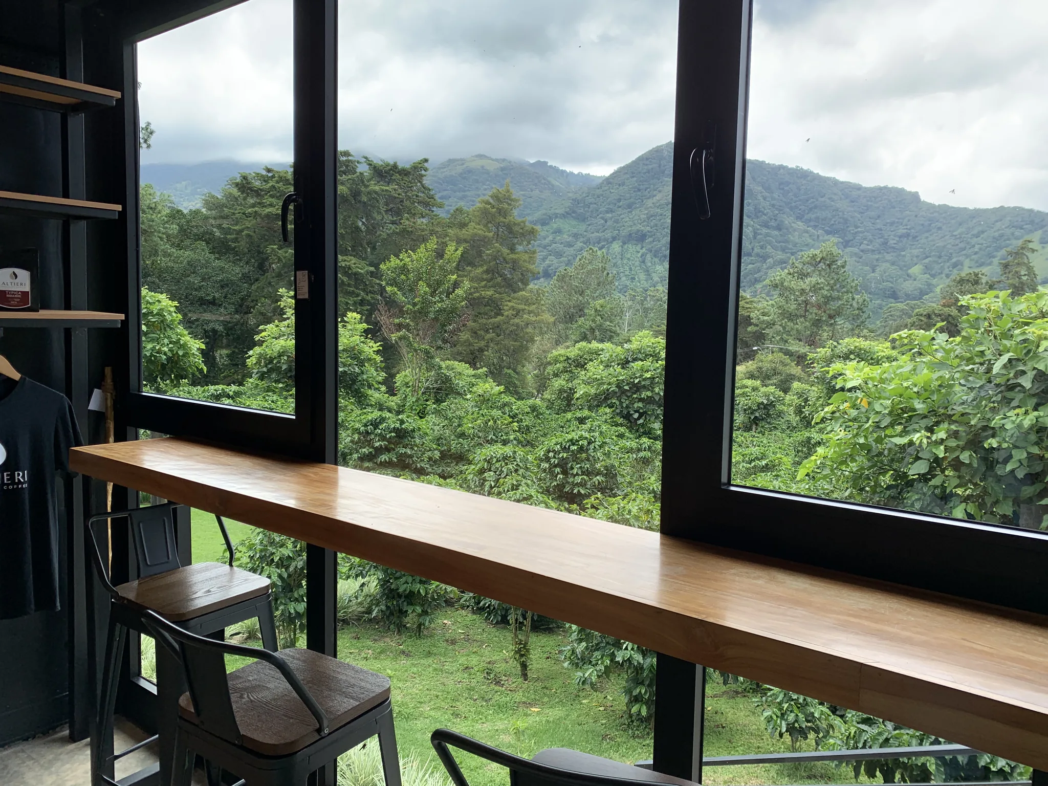 Cafetales y montañas con neblina llenan la vista desde la barra de una ventana, con mercancía de la marca colgada al lado.