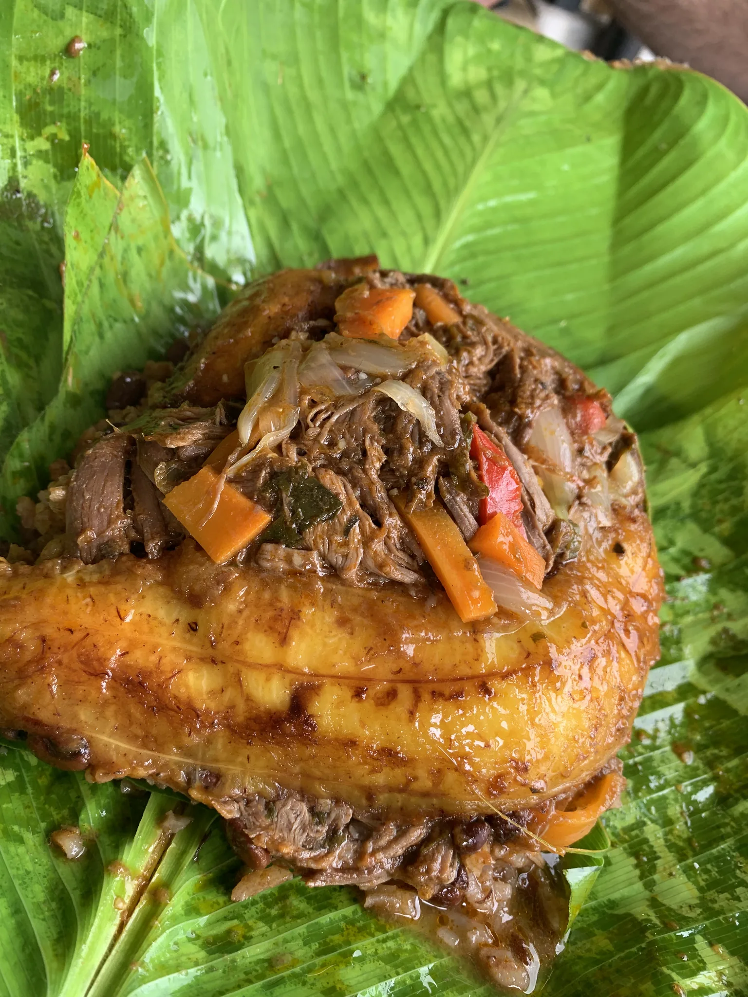 Carne deshebrada con pimentón y zanahoria corona un plátano frito, servida abierta sobre una hoja de bijao.