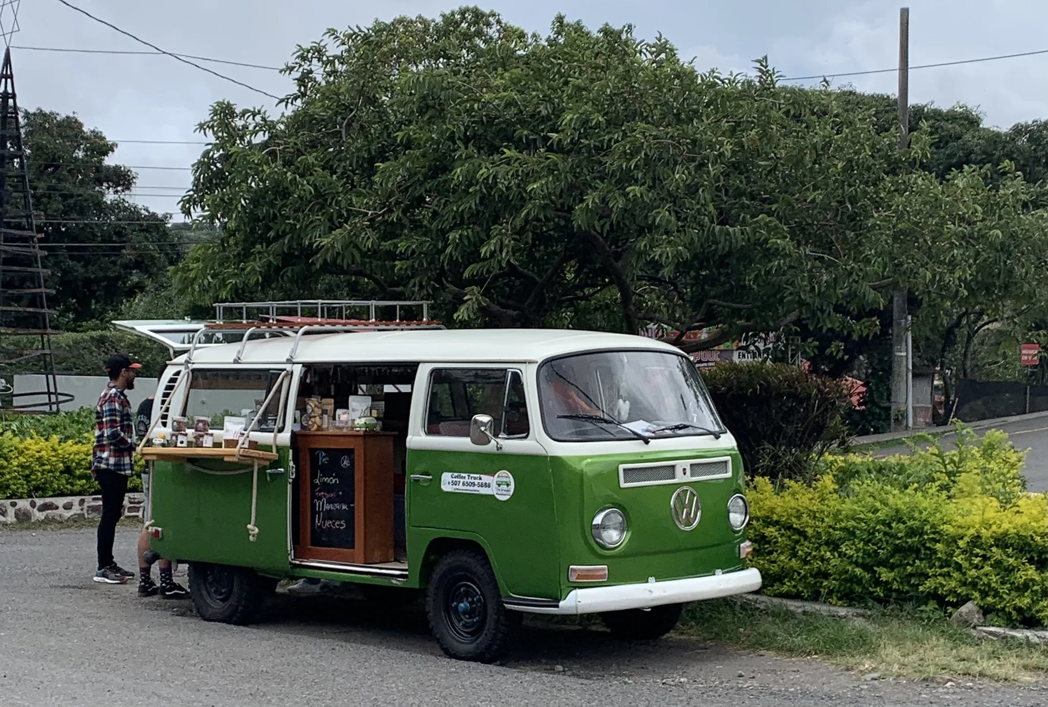 A green vintage VW van converted into a roadside coffee stand, its side hatch open and a chalkboard menu on display.
